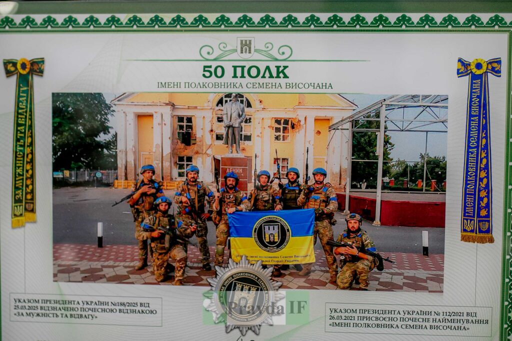 Військовий підрозділ перед пошкодженою будівлею з прапором.
