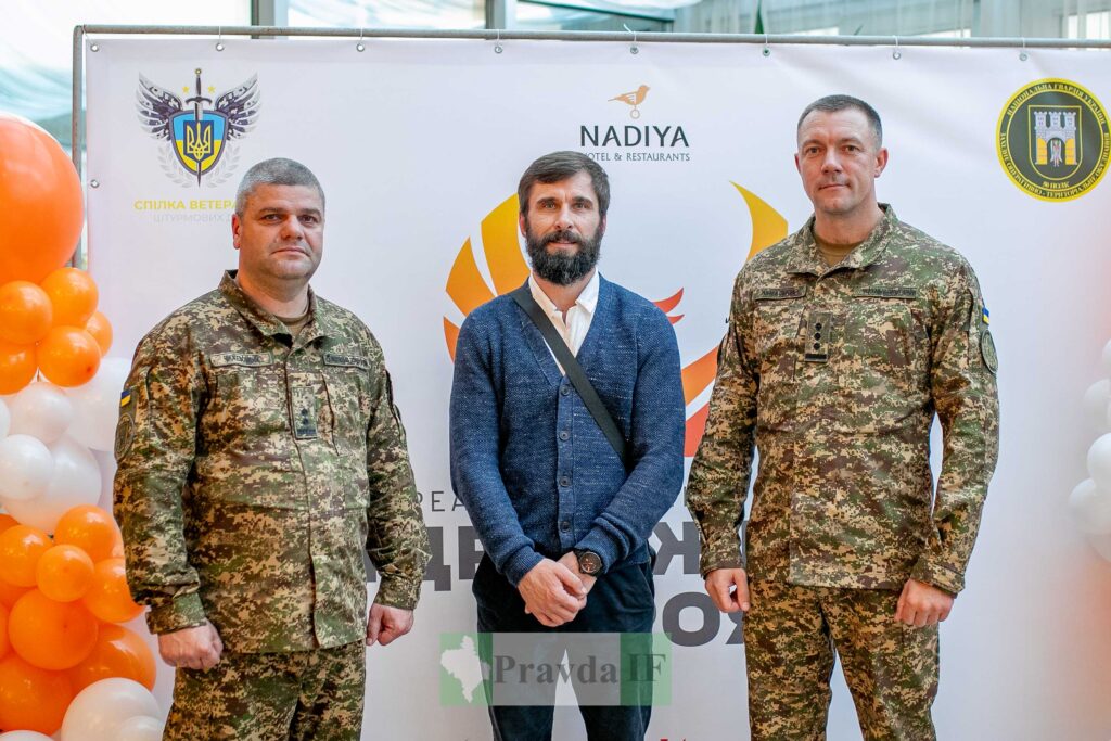 Три чоловіки перед банером, двоє у військовій формі.