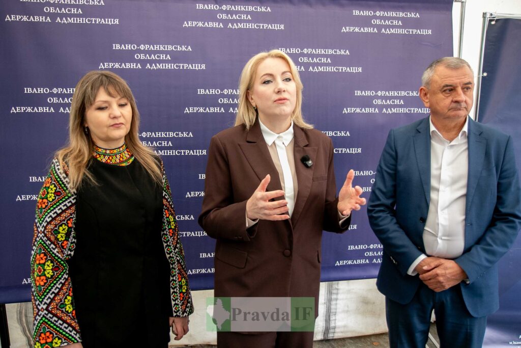 Три людини на фоні банера Івано-Франківська.