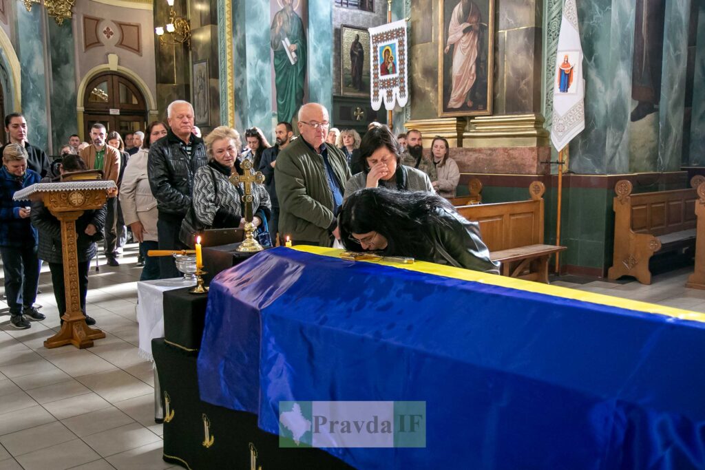Люди вшанують труну з українським прапором у церкві.