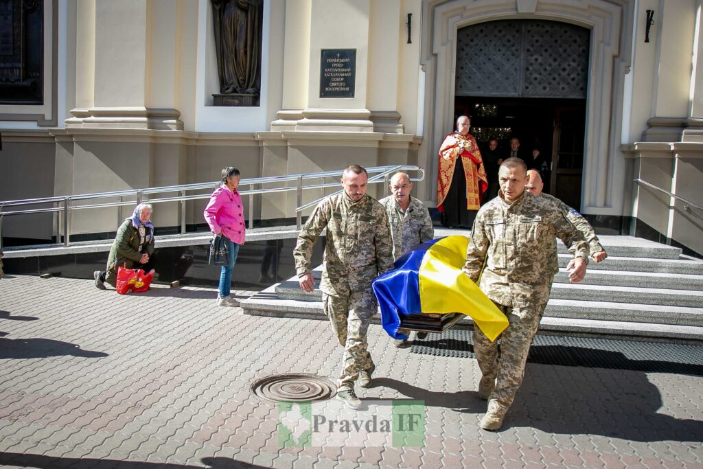Військові несуть труну, покриту українським прапором.