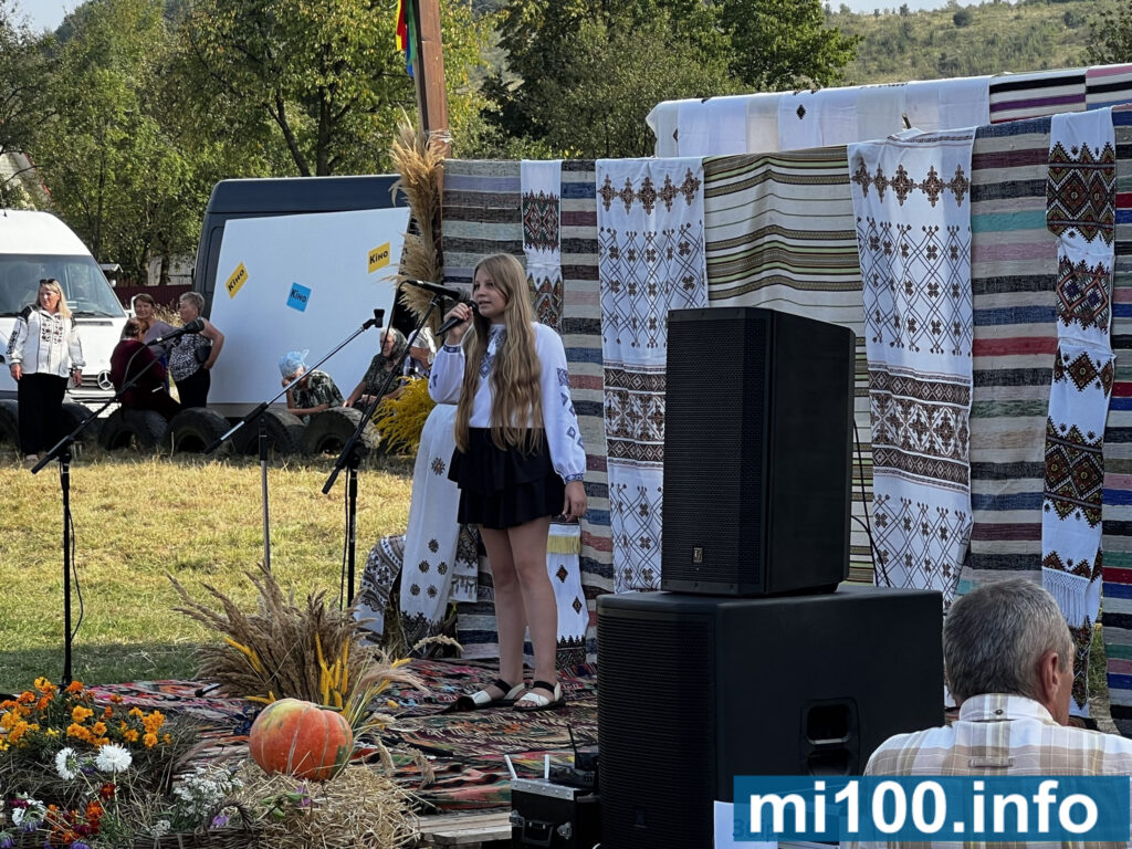 Дівчина співає на сцені з вишитими рушниками.