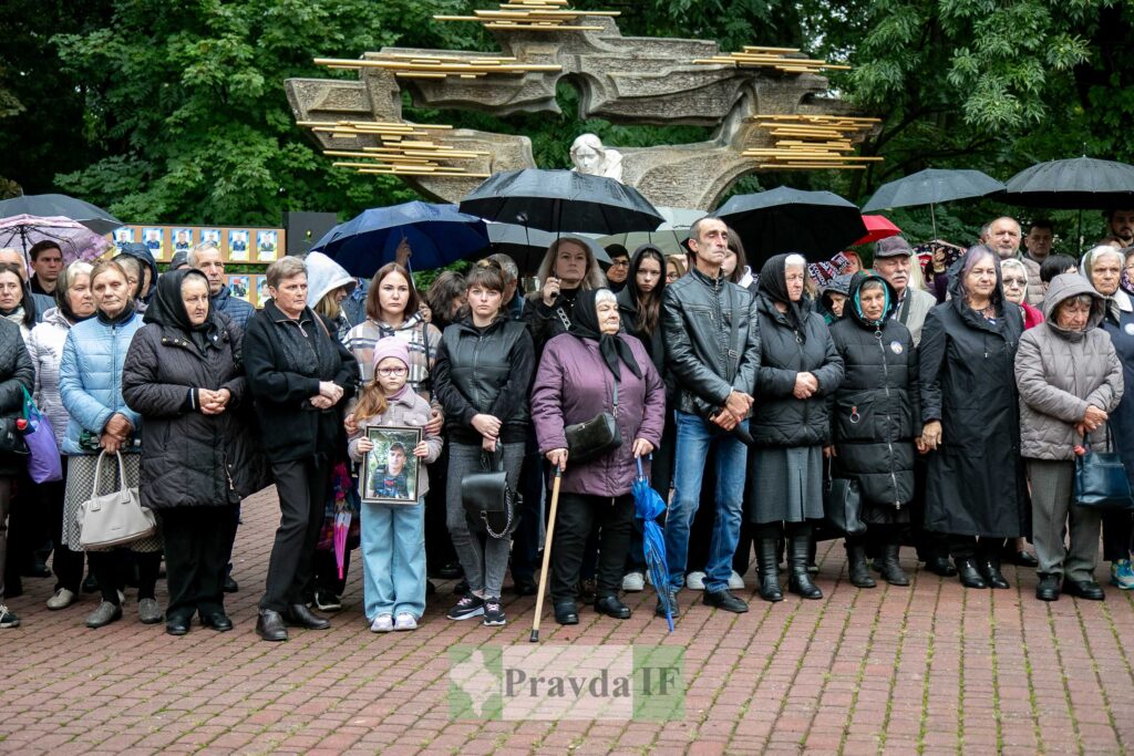 Люди на мітингу під дощем з парасольками.