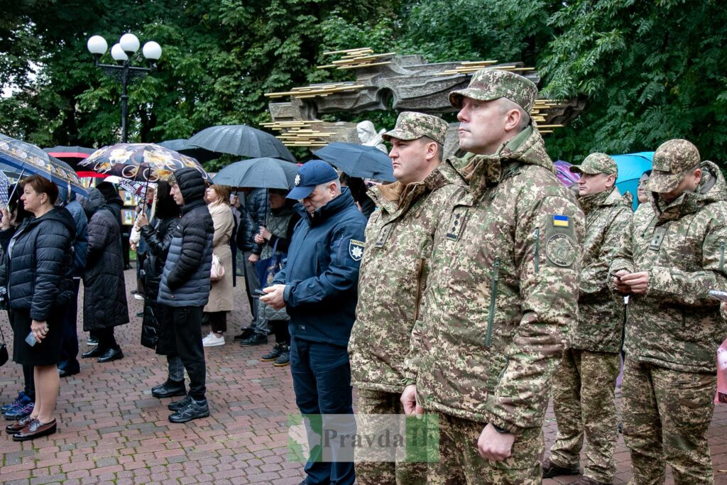 Люди під парасольками та військові на церемонії.