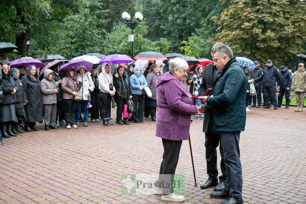Церемонія вручення нагороди під дощем, натовп під парасолями.