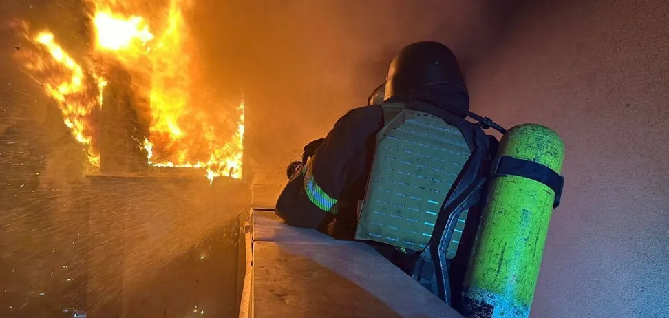 Пожежник гасить пожежу у багатоповерхівці вночі.