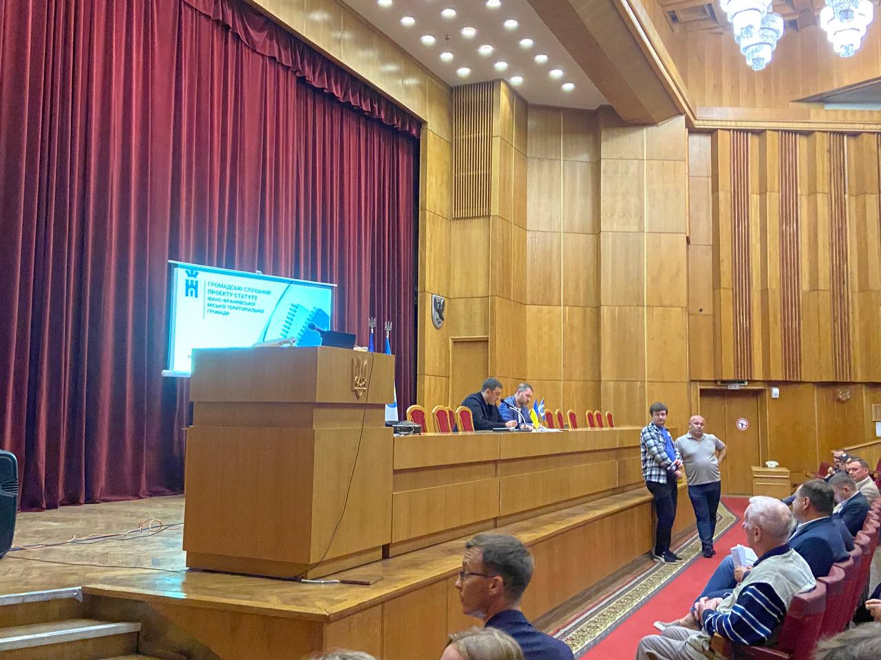 Громадські слухання в актовій залі з проєкційним екраном.