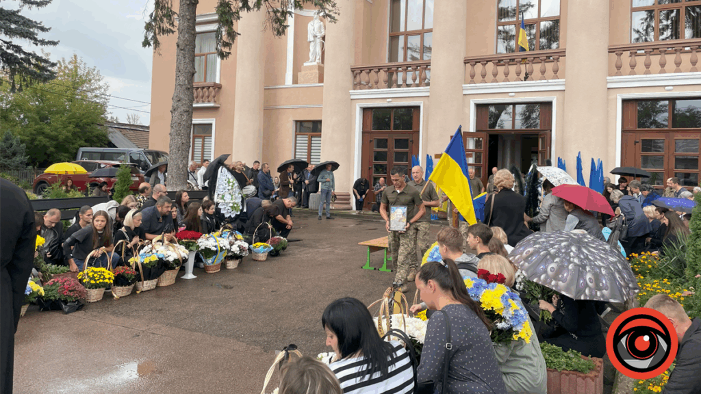 Люди на вулиці з українськими прапорами та квітами.