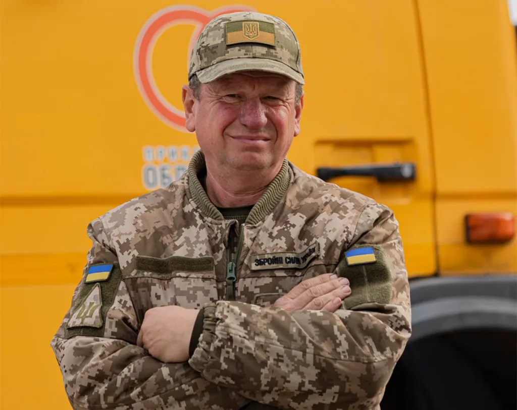 Український військовий у камуфляжі перед жовтим транспортом