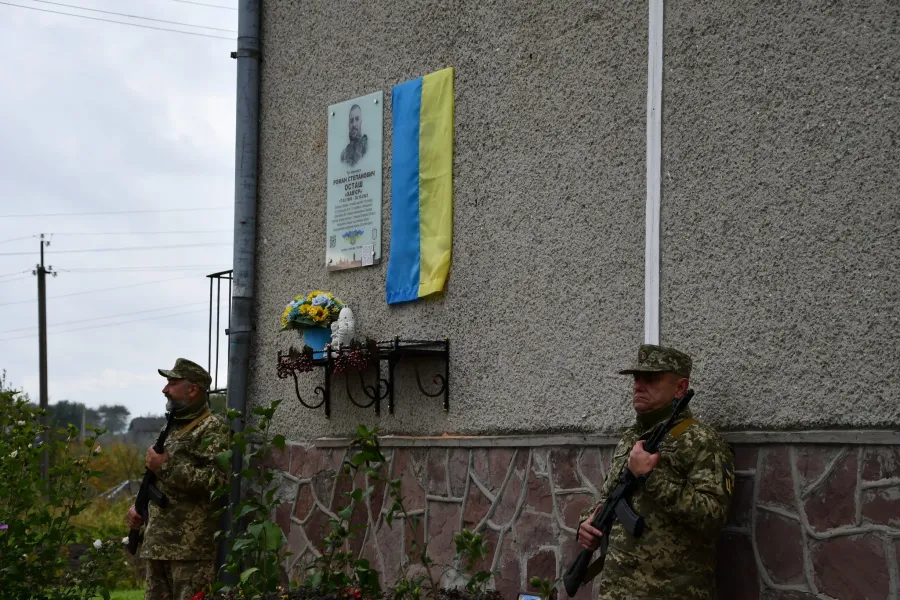 Військові стоять біля меморіальної дошки та прапора України