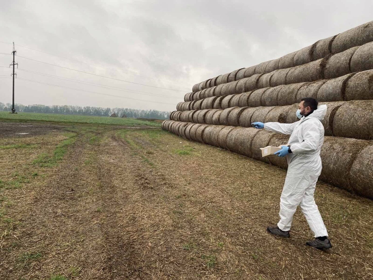 Чоловік в захисному костюмі біля сіна на полі.