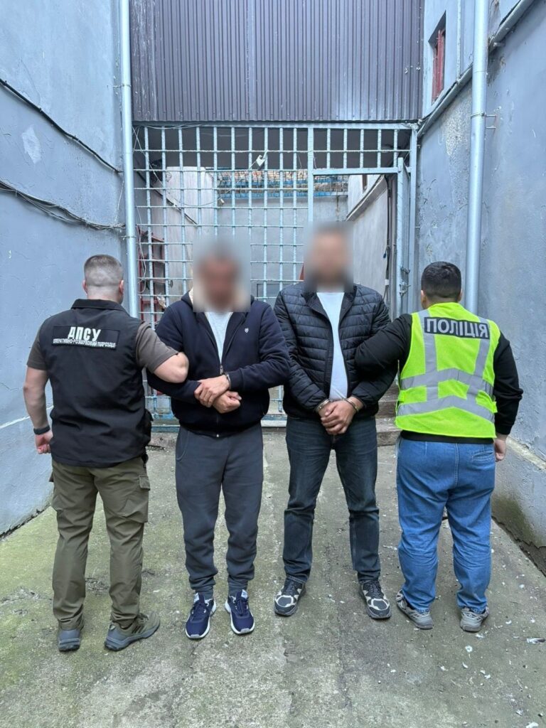 Поліція затримує двох підозрюваних чоловіків біля ґрат.