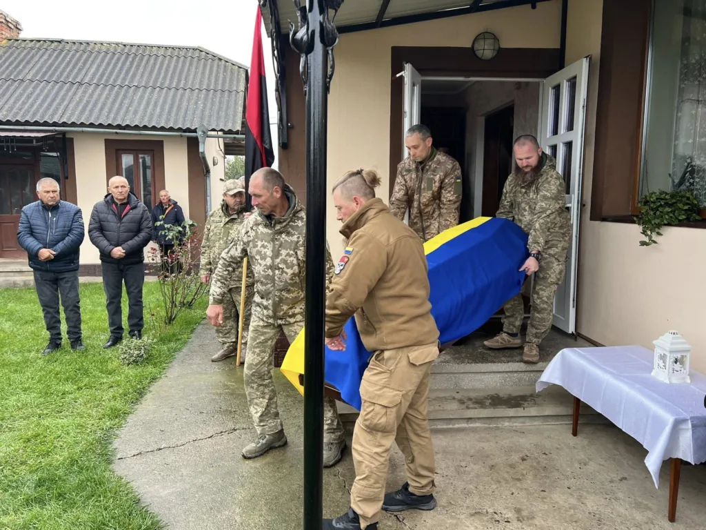 Військові несуть труну, накриту українським прапором.