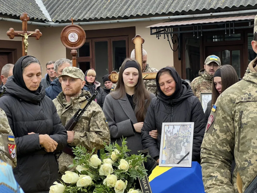 Українські солдати на похороні з прапором і квітами.