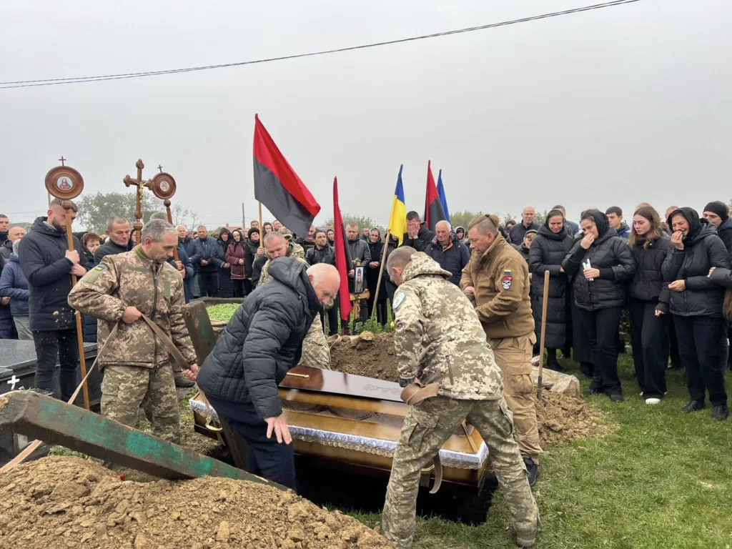 Військовий похорон із прапорами та людьми навколо.