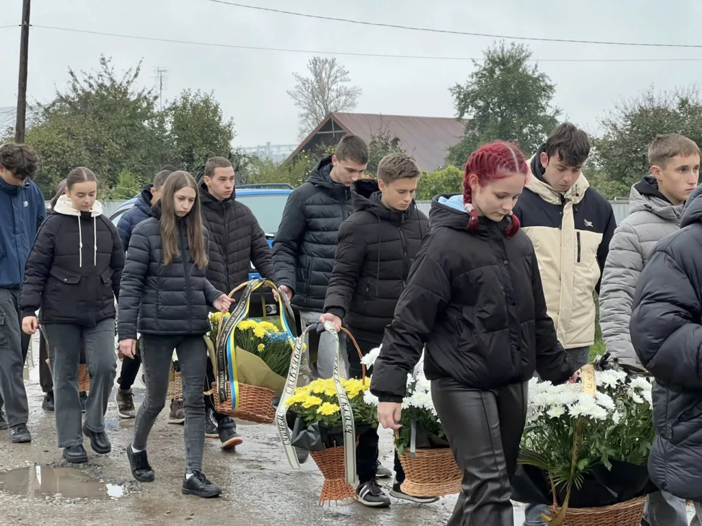 Люди несуть квіти на вулиці в похмурий день.