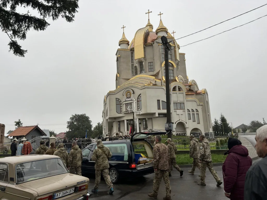 Військові біля церкви з жовтими куполами в селі.