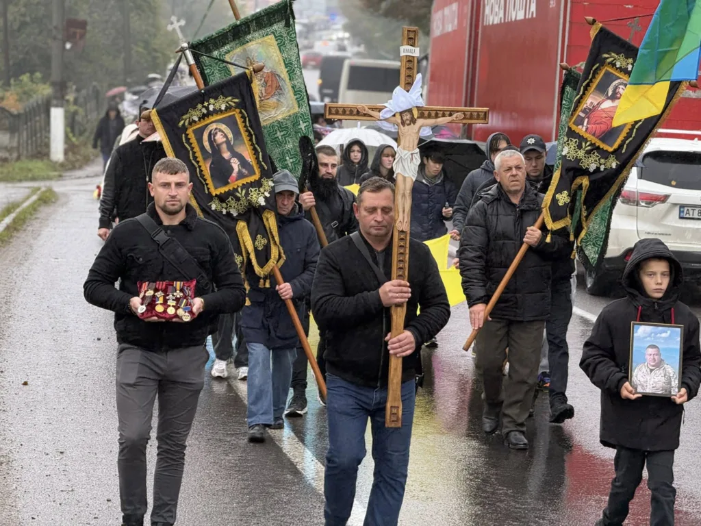 Похоронна хода з хрестом і прапорами в дощ.