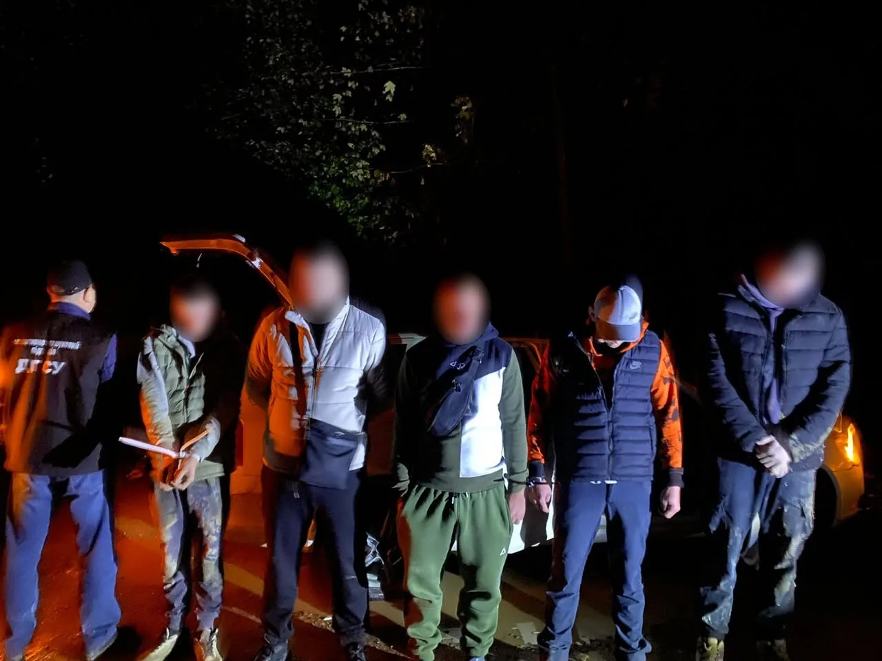 Група людей біля автомобіля вночі.