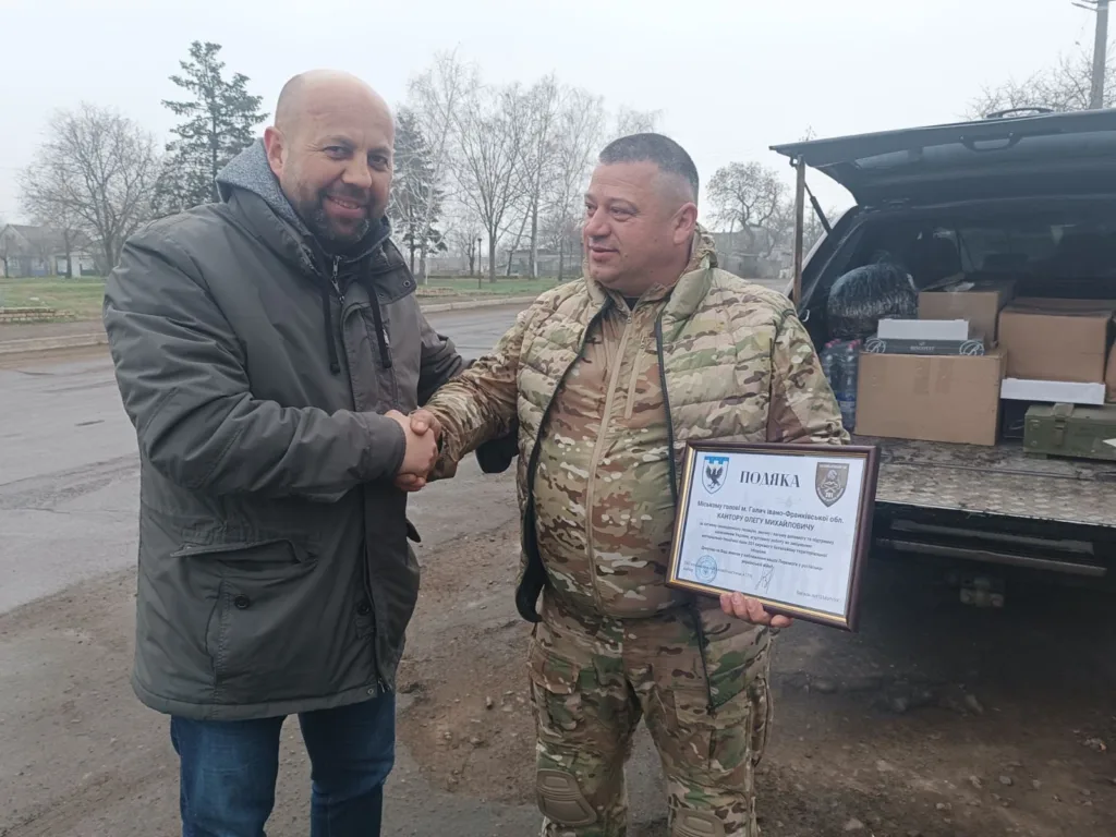 Двоє чоловіків тиснуть руки, один тримає подяку.