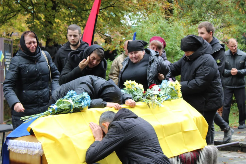 Люди оплакують полеглого воїна під українським прапором
