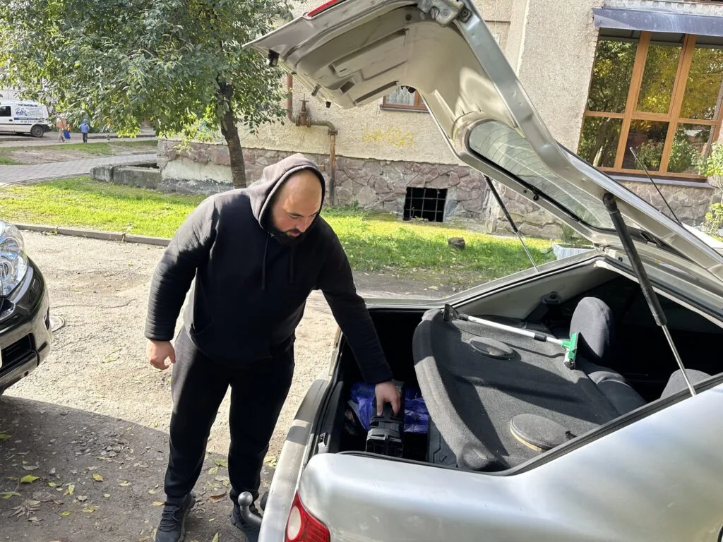 Чоловік кладе річ у багажник автомобіля