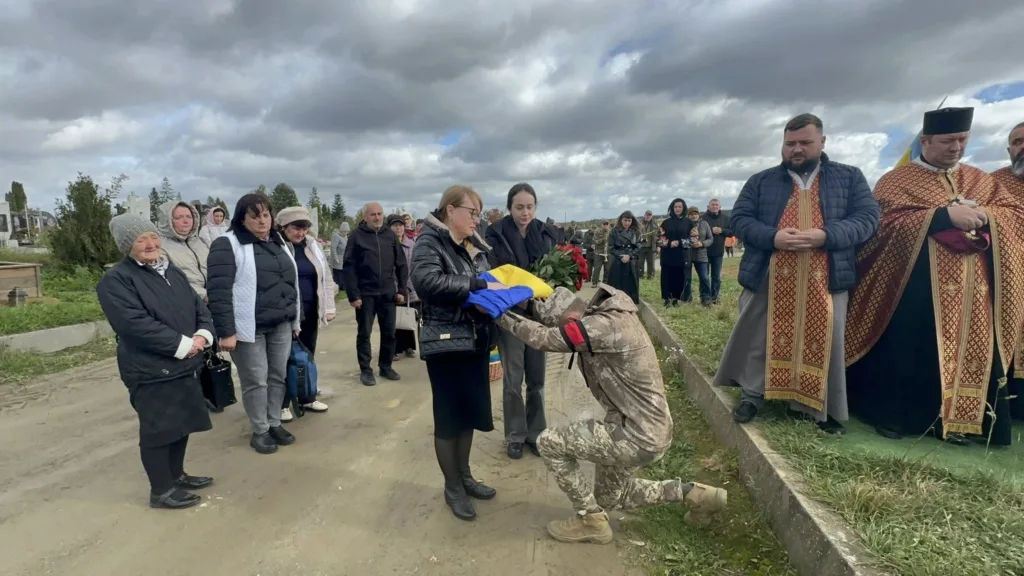 Військовий на колінах перед українським прапором на похороні