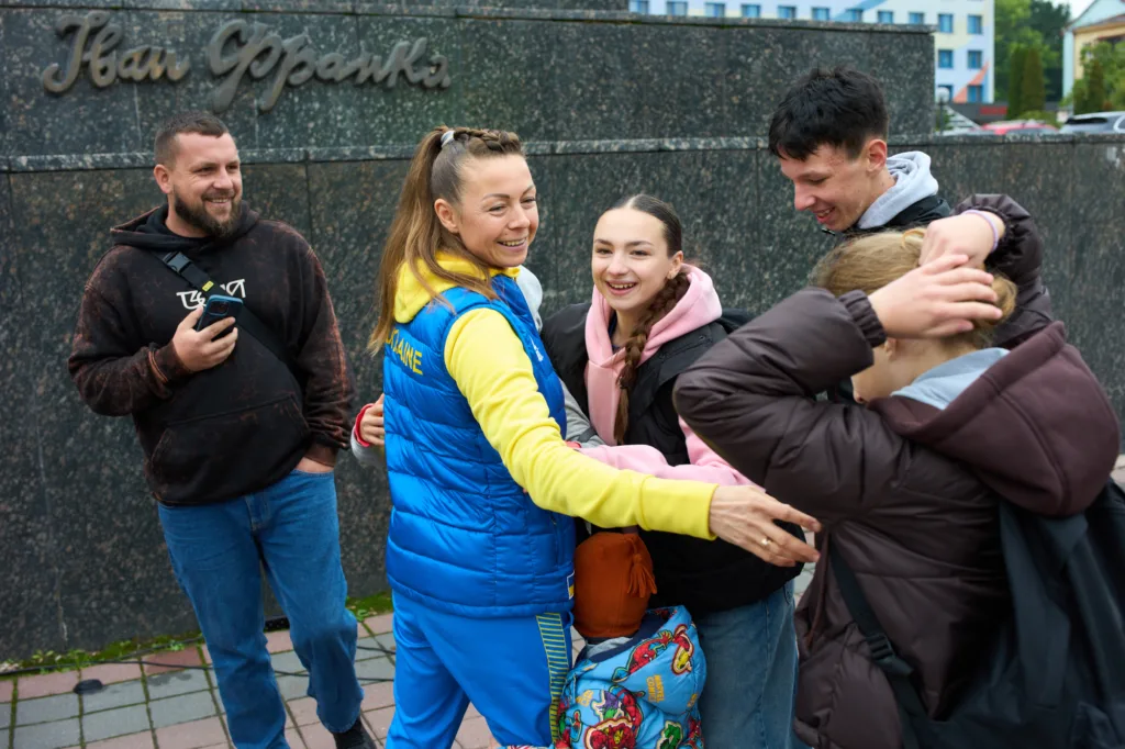 Група людей обіймається на вулиці, поруч пам'ятник.