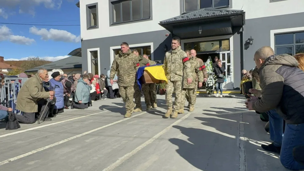 Військові несуть труну, люди стоять на колінах