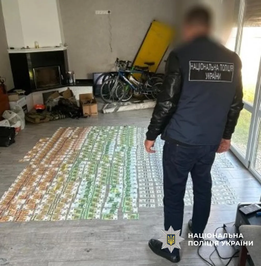Поліцейський оглядає вилучені гроші в будинку