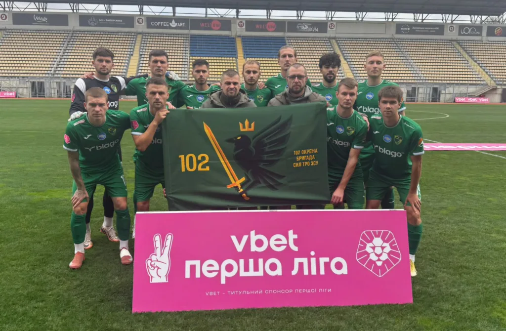 Футбольна команда позує з прапором на стадіоні