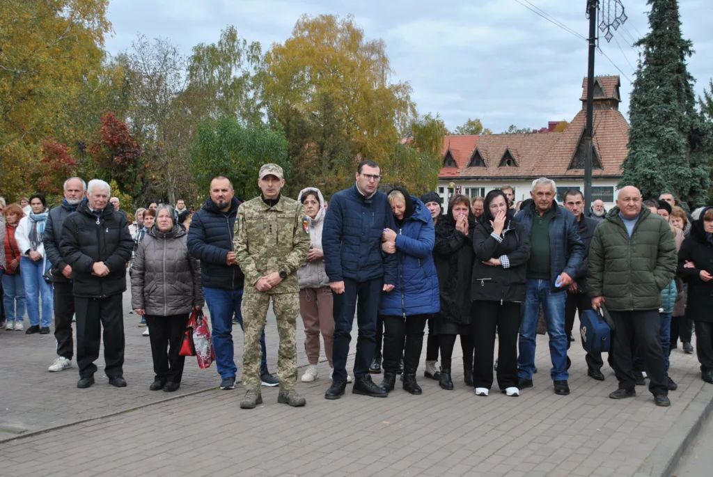 Люди стоять під час церемонії вшанування героя.