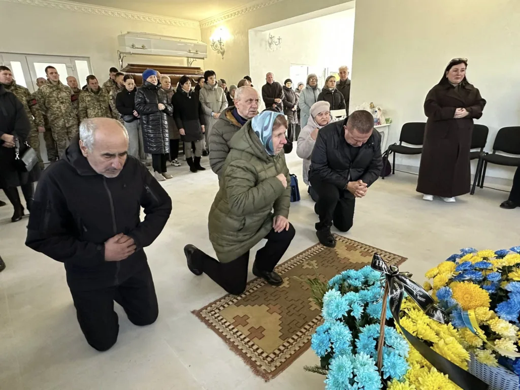 Люди моляться біля труни на прощанні з військовим.