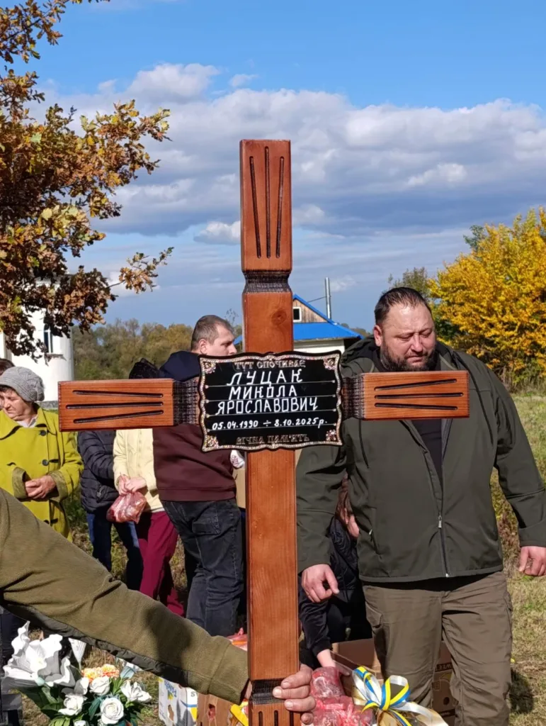 Люди на цвинтарі тримають дерев'яний хрест