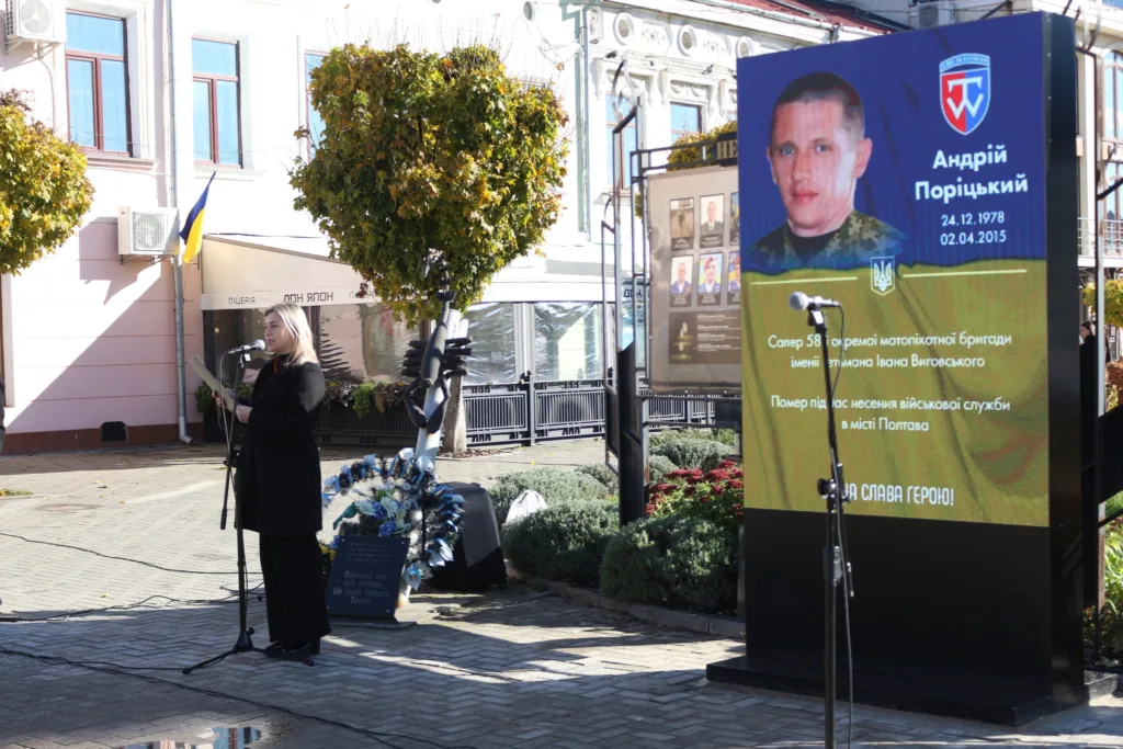 Жінка виступає біля меморіального екрана героя