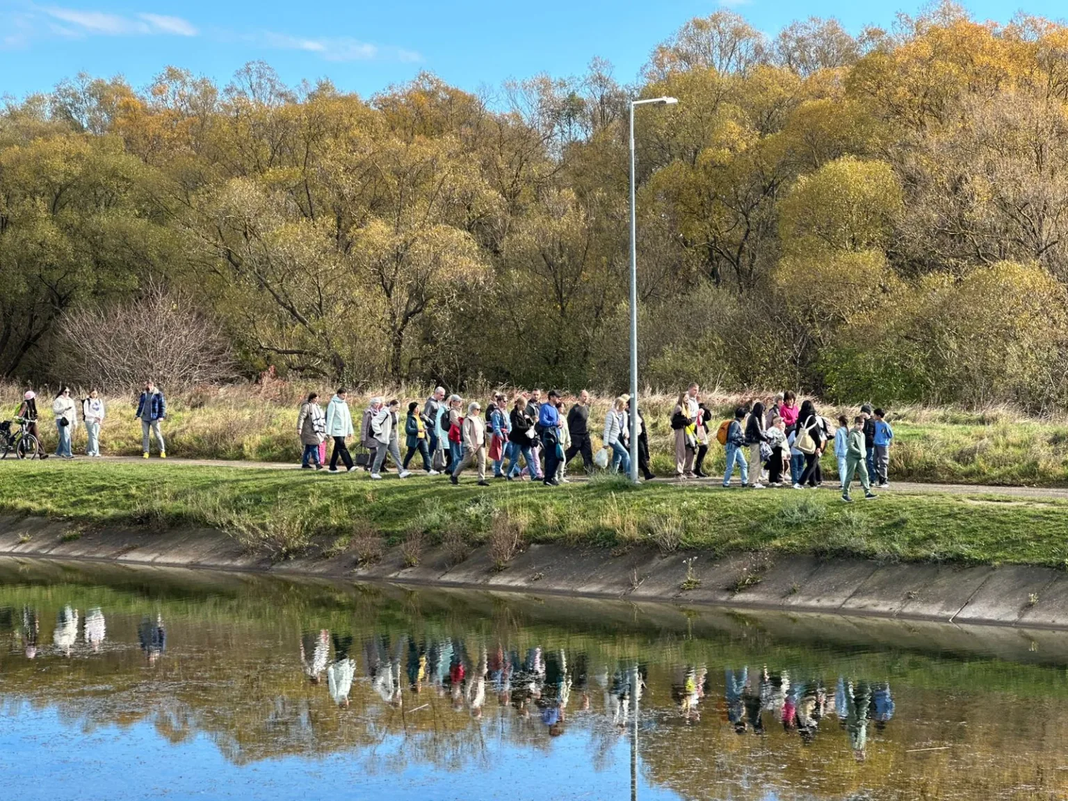 Група людей гуляє біля річки восени