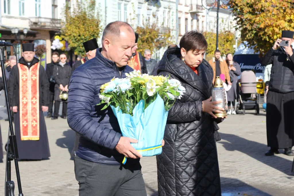 Люди несуть квіти та свічку на церемонії