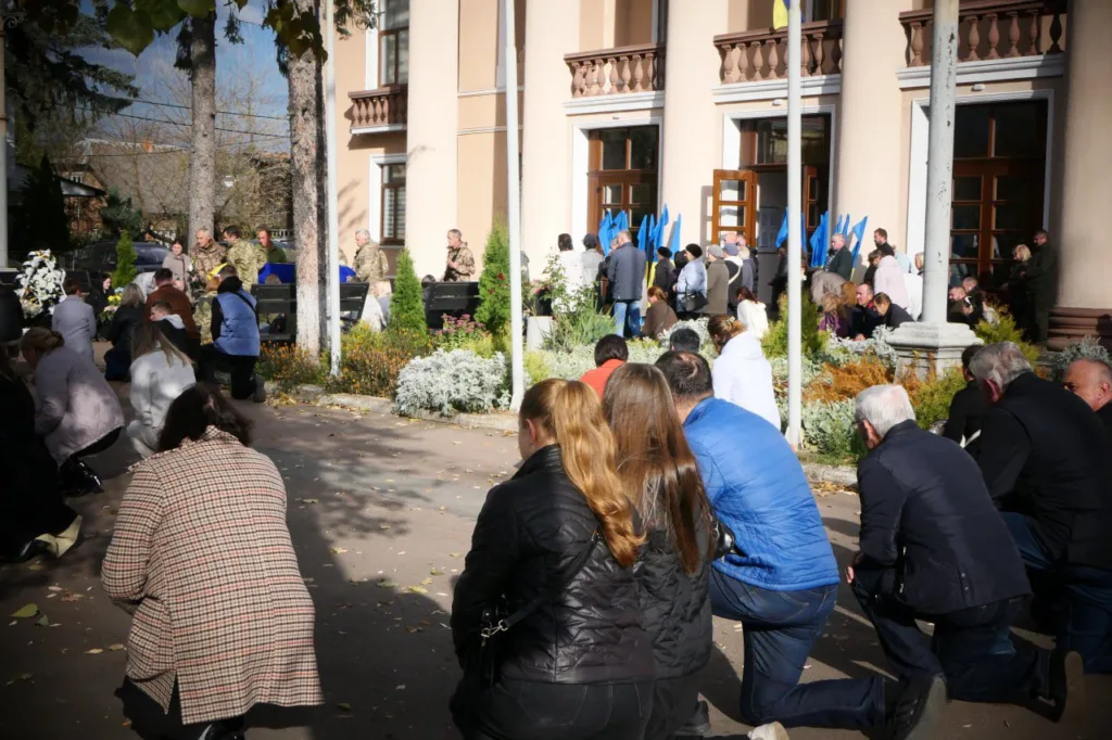 Люди на колінах під час церемонії біля будівлі