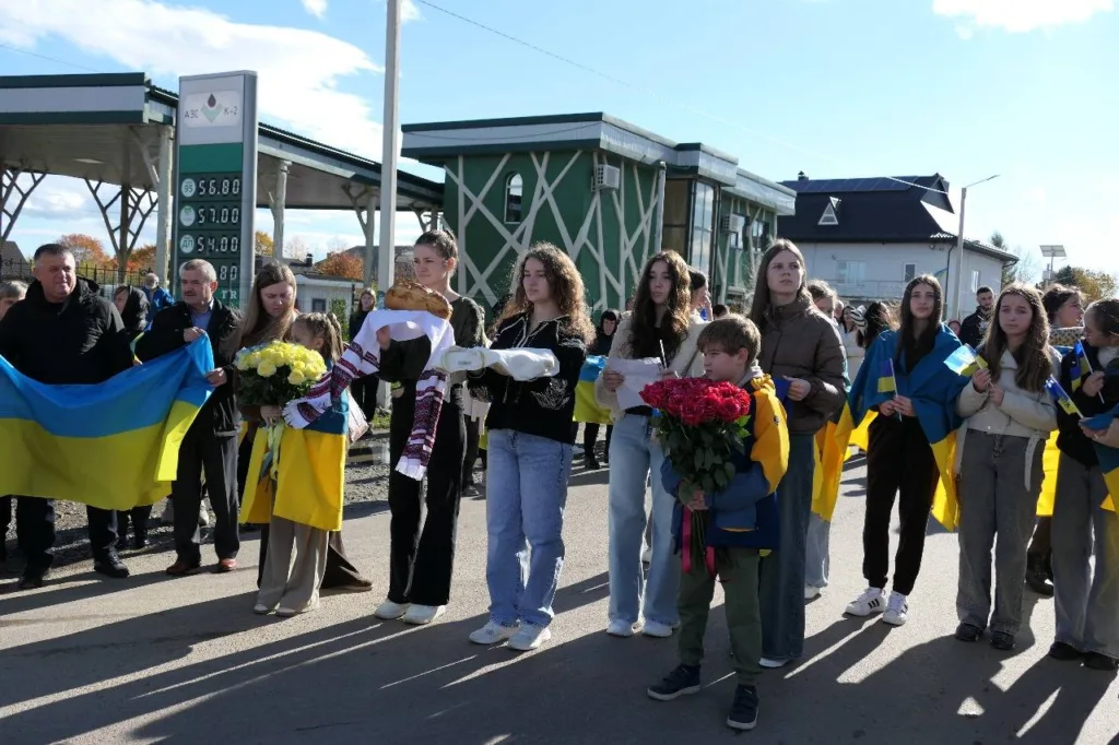 Люди з українськими прапорами та квітами на вулиці