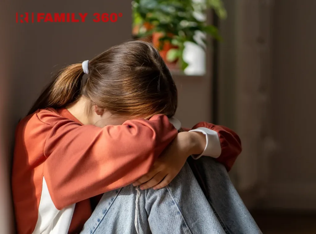 Сумна дівчина сидить, обхопивши коліна руками