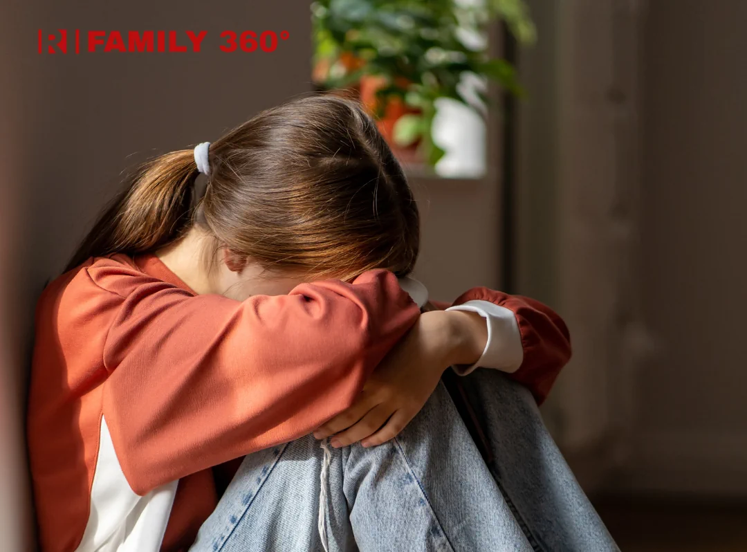 Сумна дівчина сидить, обхопивши коліна руками