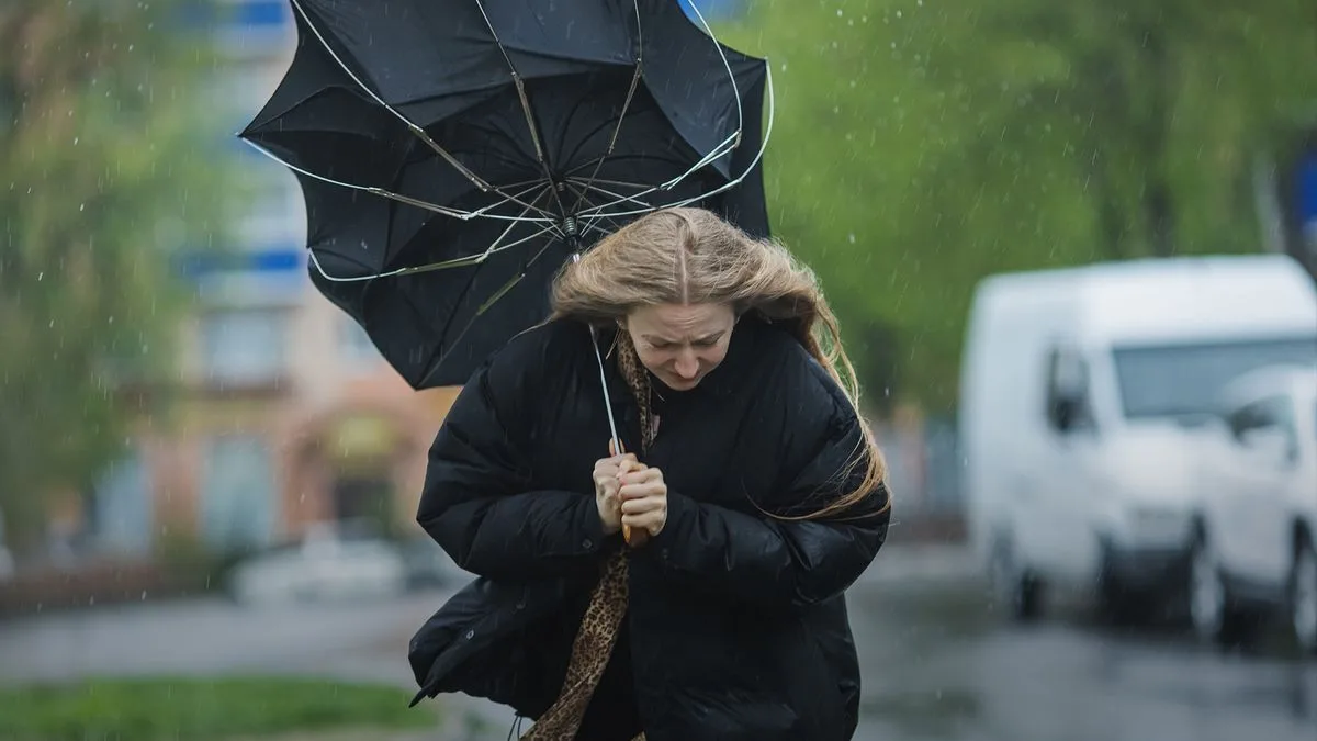 Жінка бореться з вітром і дощем під парасолькою