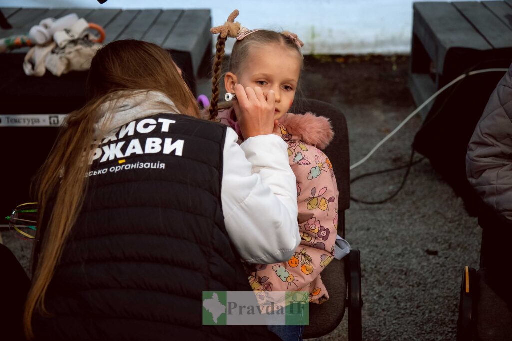 Дівчинка, на обличчі якої малює волонтер.