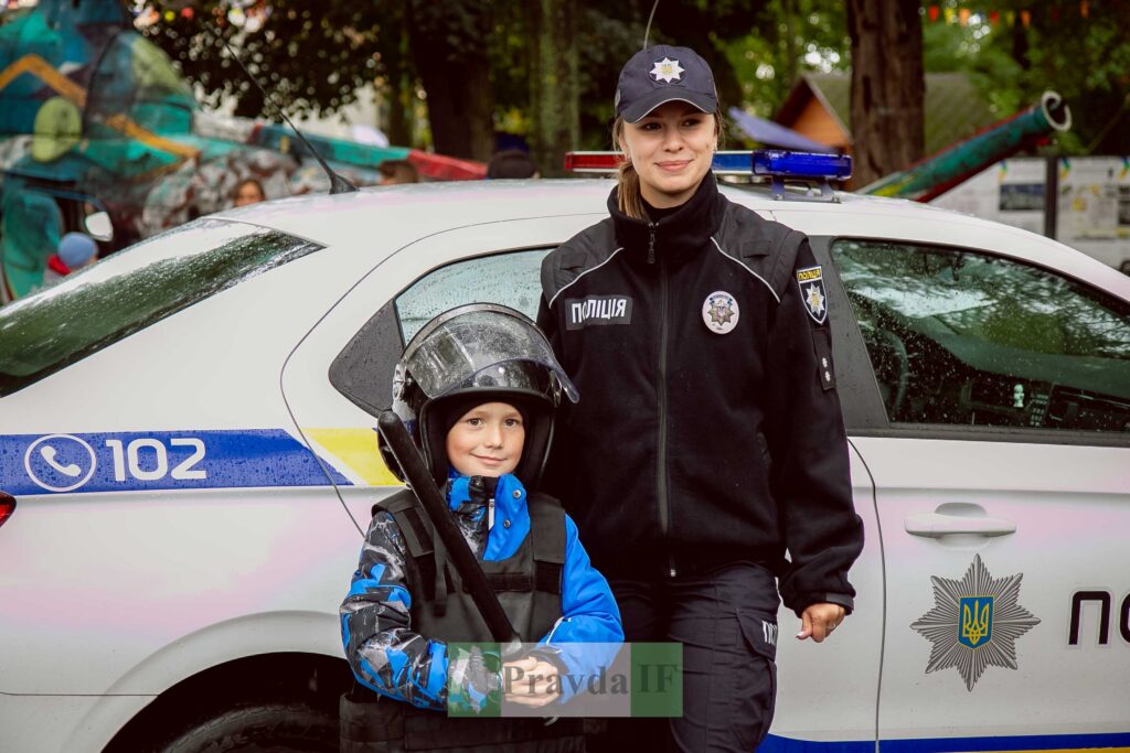 Дитина та поліцейська біля машини поліції.
