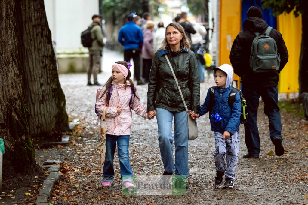 Жінка з двома дітьми гуляють парком восени.