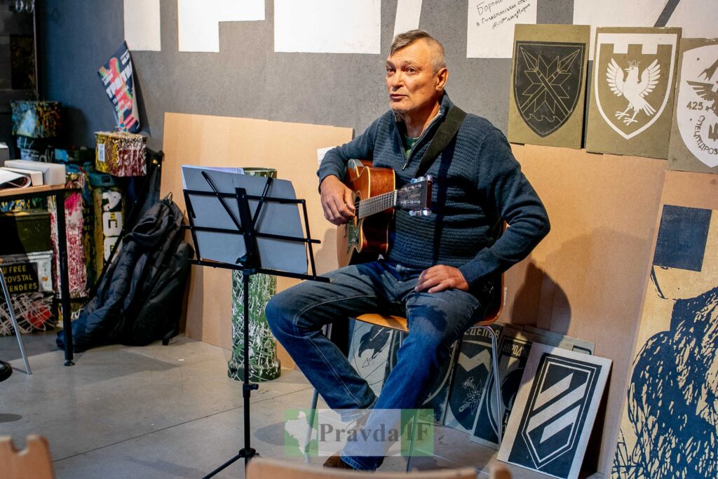 Чоловік з гітарою у кімнаті зі стінами мистецтва.