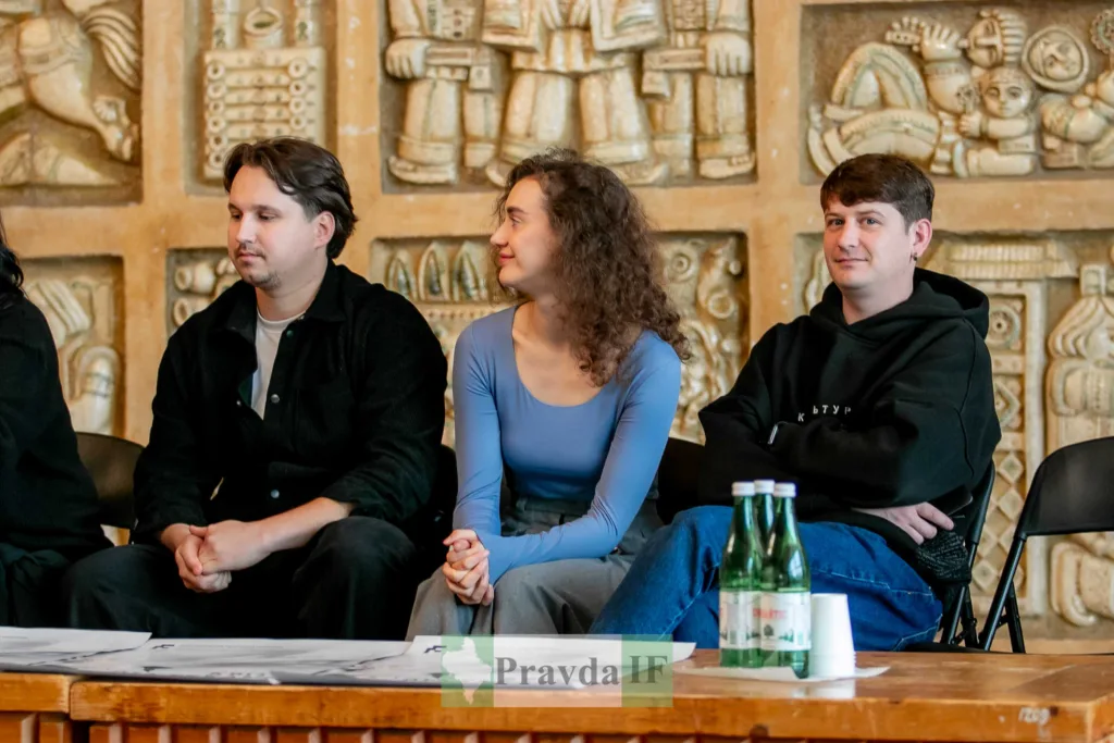 Люди сидять перед декоративною стіною в залі