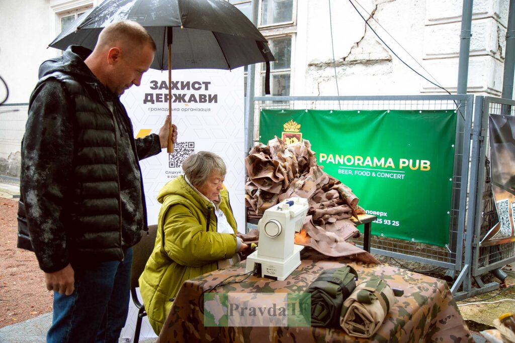 Літня жінка шиє маскувальні сітки на вулиці.
