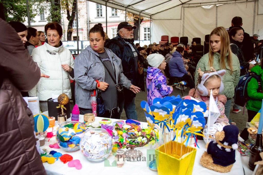 Люди на ярмарку з українськими сувенірами та іграшками.