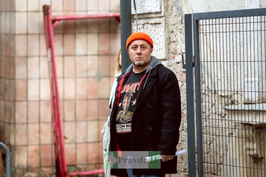 Чоловік у червоній шапці стоїть біля стіни.